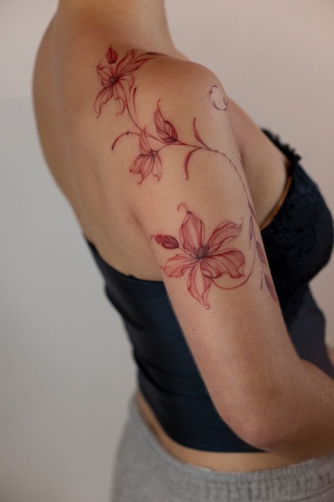 Czerwony tatuaż fineline z motywem kwiatowym na ramieniu wykonany w Częstochowie.