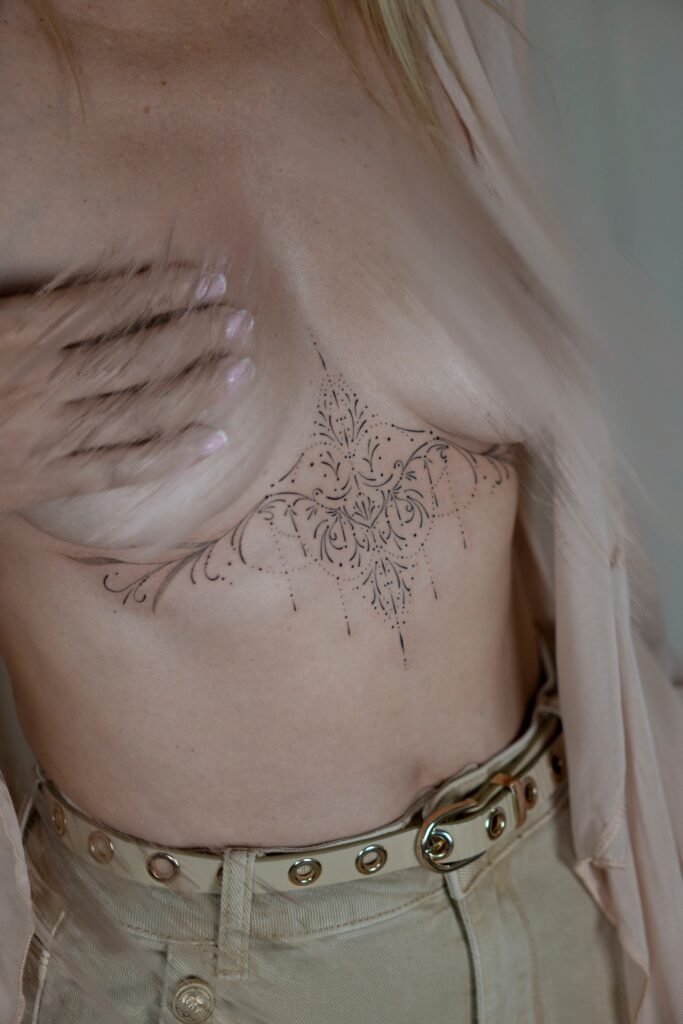 Delikatny tatuaż ornamentalny fineline na mostku pod biustem wykonany w Częstochowie.