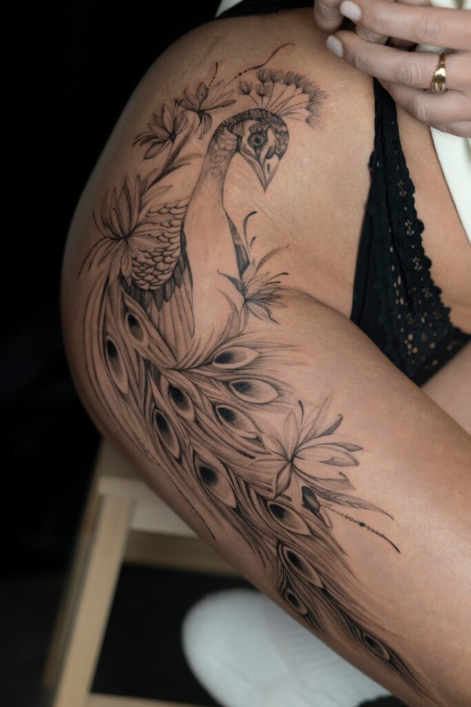 Artystyczny tatuaż przedstawiający pawia z motywem botanicznym na biodrze wykonany w Częstochowie.