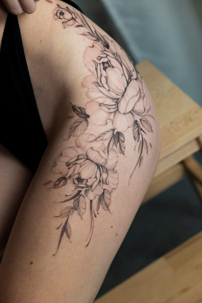 Delikatny tatuaż piwonie w technice fineline na górnej części uda wykonany w Częstochowie.