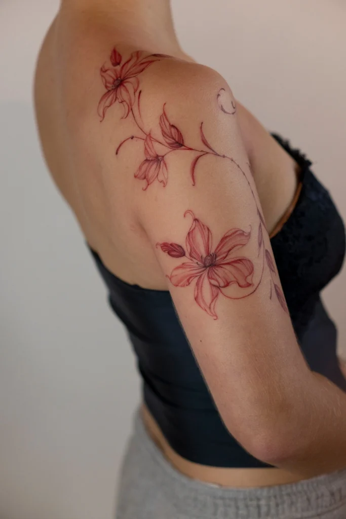 Delikatny czerwony tatuaż kwiatowy na ramieniu wykonany techniką cienkiej linii fineline.