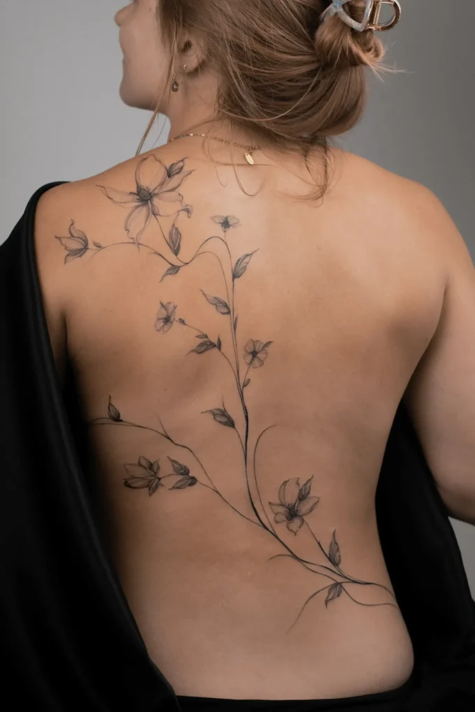 uży, subtelny tatuaż botaniczny na plecach kobiety, przechodzący od łopatki w dół, wykonany techniką cienkiej linii fineline przez Wikę Olejnik.
