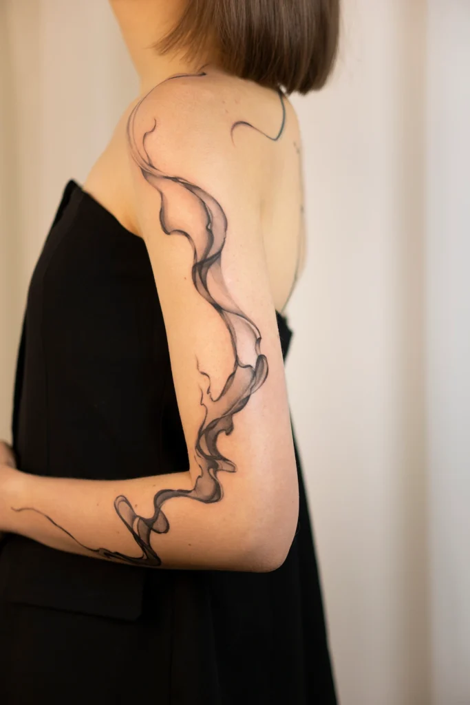 Abstrakcyjny tatuaż w formie dymu na ramieniu i przedramieniu – delikatny czarny tatuaż Częstochowa