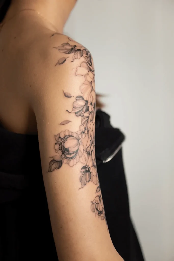 Kobiecy tatuaż fineline na ramieniu przedstawiający piwonie i pąki kwiatów z delikatnym cieniowaniem. Projekt wykonany przez Wikę Olejnik w Częstochowie.